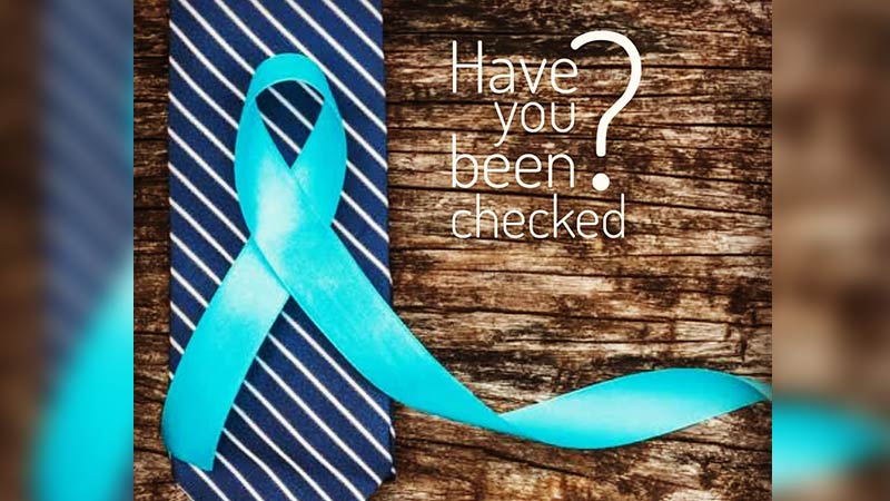 blue ribbon prostate awareness poster asking 'have you been checked?' which features a blue tie with white stripes sitting on a rough timber table with a light blue ribbon overlaid